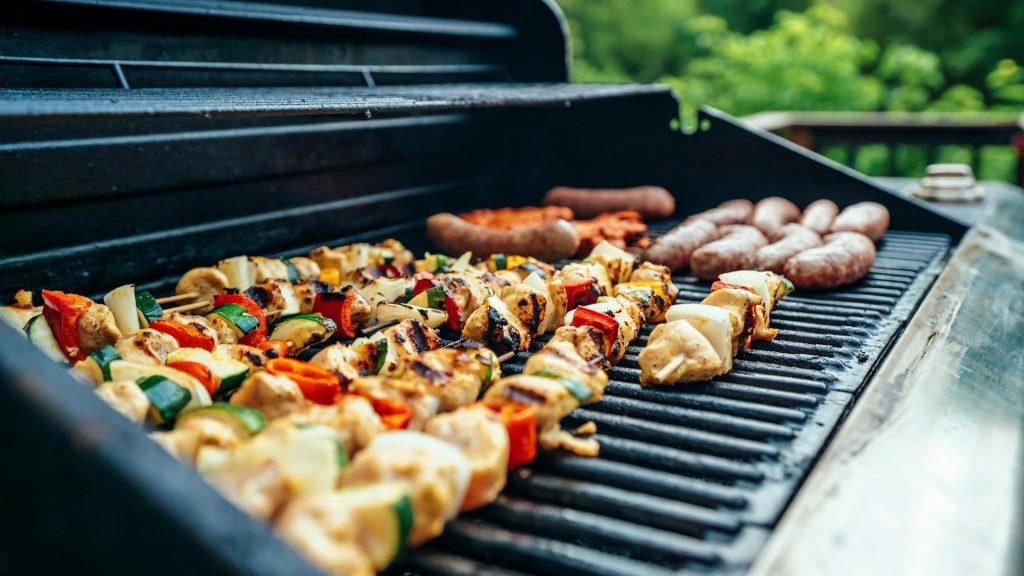 Gegrilde spiesen en worsten op een barbecue met kleurrijke groenten – bbq vlees bestellen