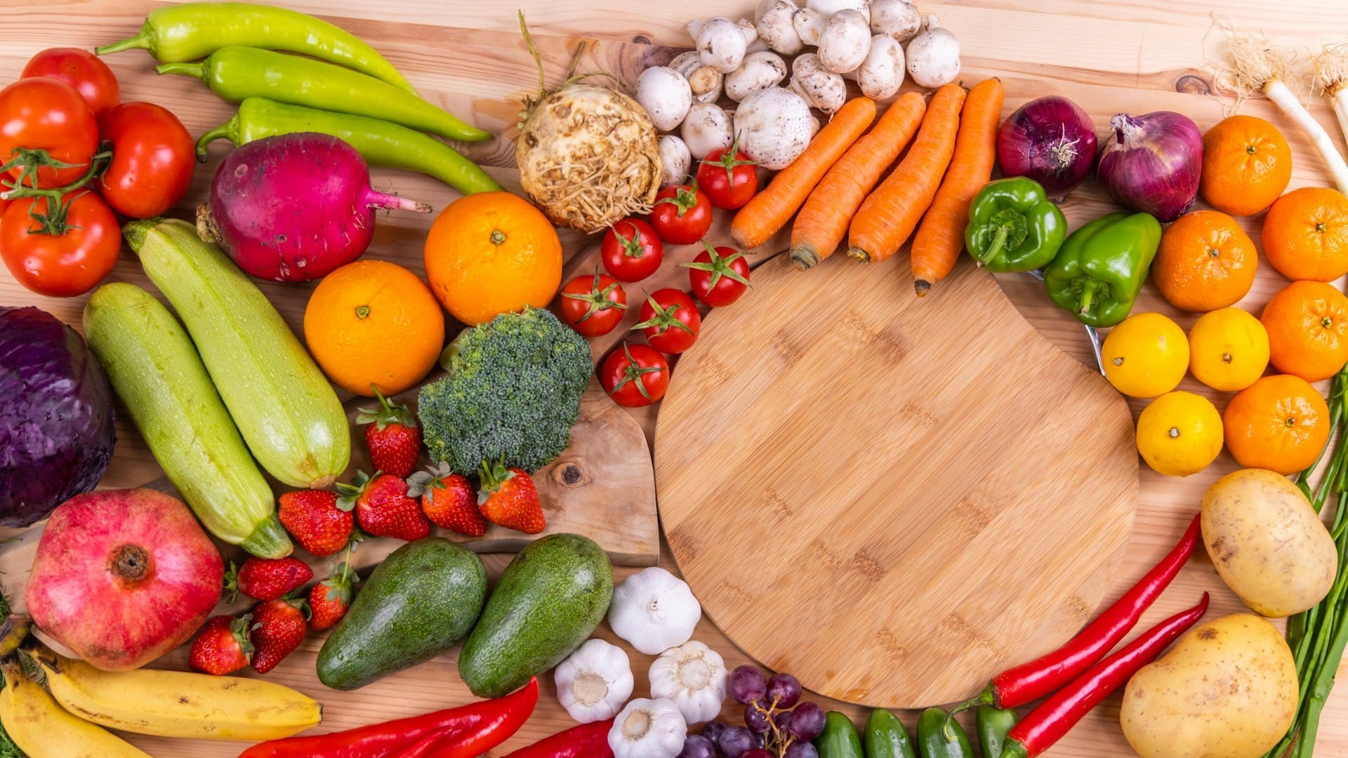 Groenten bereiden met verse ingrediënten zoals wortels, paprika, broccoli en courgette rondom een houten snijplank.