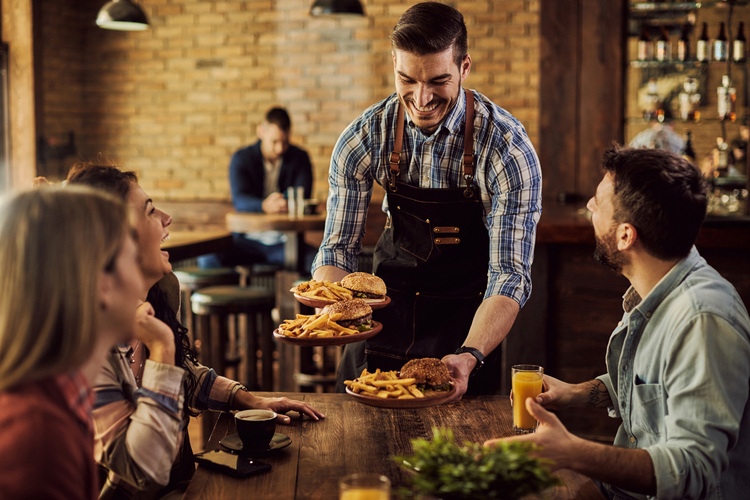 Ober serveert burgers met friet aan vriendengroep in restaurant.