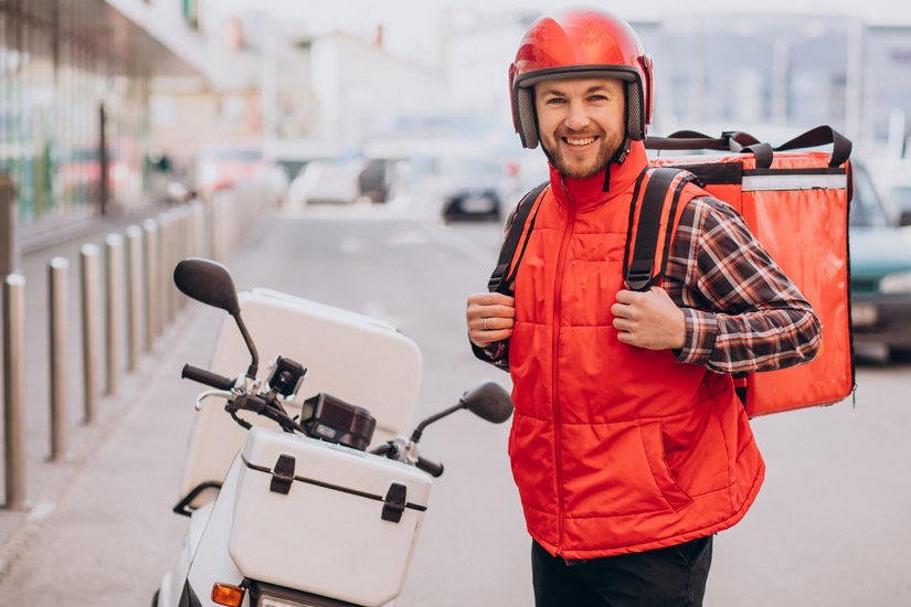 Koerier met bezorgtas staat naast scooter voor het bezorgen van eten.