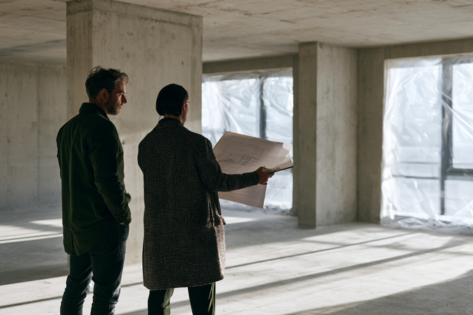 Architect en klant bekijken een bouwtekening in een lege horeca nieuwbouwruimte.